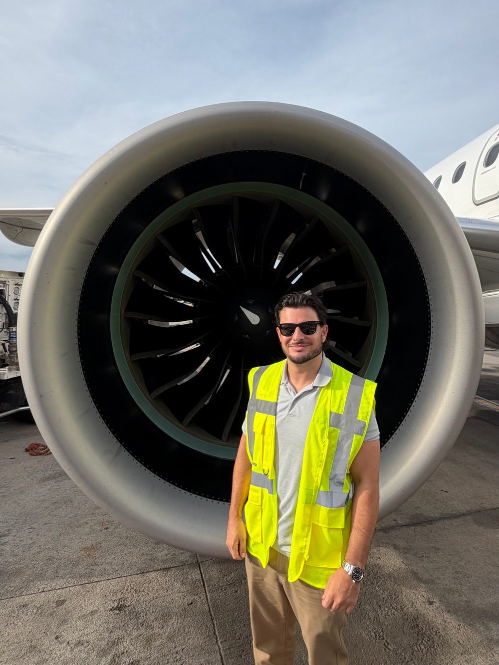 Sam standing on the ramp in front of a jet engine, in a hi-vis vest